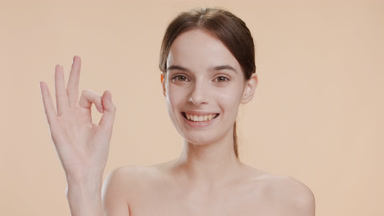 Cute young woman shows OK sign smiling wide on beige background