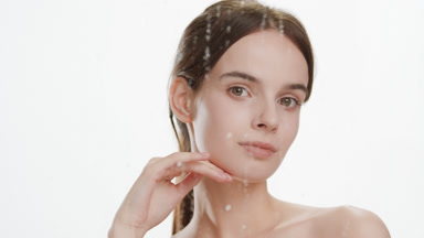 Woman strokes face and jawline turning head behind fogged glass