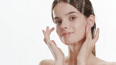 Cute slim woman strokes her face turning head behind foggy glass