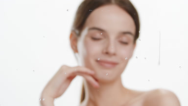 Woman strokes jawline behind glass with water drops roll down