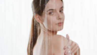Pretty woman strokes shoulder behind glass with drops roll down