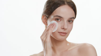 Woman strokes face using cotton pad smiling behind foggy glass