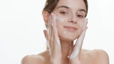 Pretty slim woman applies foam on cheeks behind glass with drops