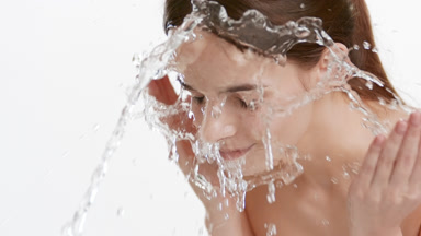 Good-looking woman with long brown hair washes her face smiling