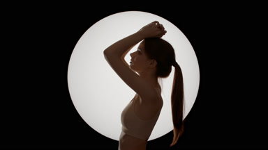 Half-turned beautiful slim woman in beige top with hands on head