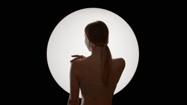 Young slim woman in beige top standing in back strokes clavicles