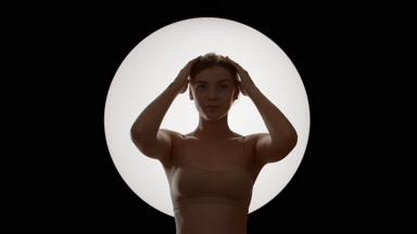 Gorgeous Caucasian woman in beige top touches hair moving head