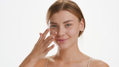Cute young slim Caucasian woman strokes cheek smiling for camera