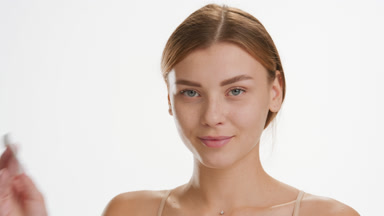 Slim woman strokes cheek using cotton pad and smiling for camera