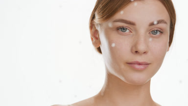 Young woman strokes nose and cheek behind glass with water drops