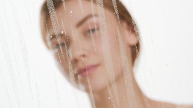 Gorgeous woman drips clear serum on cheek behind fogged glass
