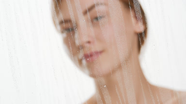 Woman drips serum on cheek and looks aside behind fogged glass