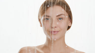 Cute woman drips serum on cheek behind glass with water drops