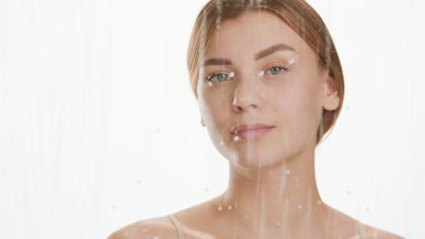 Young woman drips serum on cheek behind glass with water drops