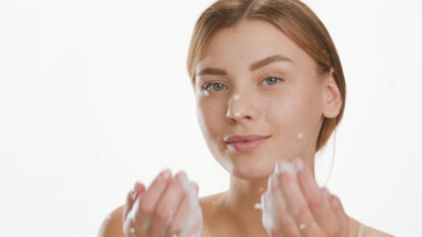 Pretty woman puts foam on cheeks behind glass with water drops