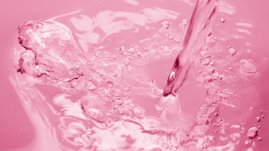 Water is pouring creating ripples and bubbles on pink background