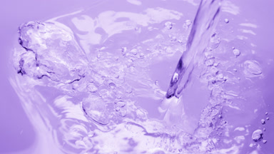 Pouring water creating ripples and bubbles on violet background