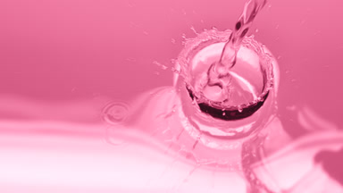 Water is poured creating ripples and bubbles on pink background