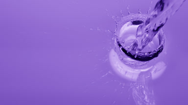 Pouring water creates ripples and bubbles on purple background