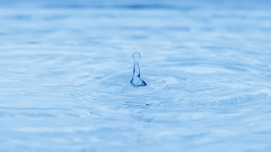 Drops fall on water surface creating rings on blue background