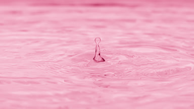 Drops fall on water surface creating rings on pink background
