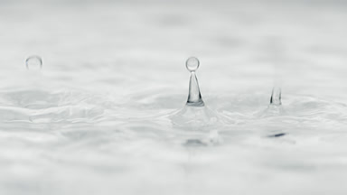 Water drops drip on water creating circles on grey background