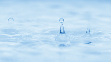 Water drops drip on water creating circles on blue background