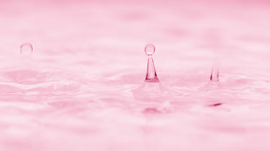 Water drops drip on water creating circles on pink background