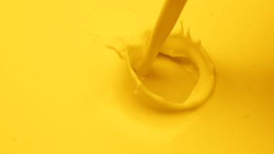 Macro of yellow liquid is poured splashing on yellow background