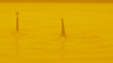Yellow opaque fluid is dripped splashing on yellow background