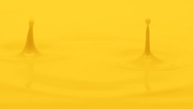 Yellow liquid is dripped creating ripples on yellow background