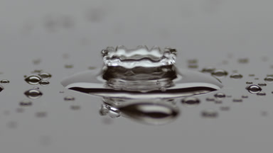 Small drop falls down on big one splashing on grey background