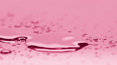 Small drop falls down near big one merging on pink background