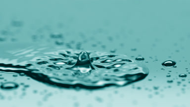 Small drop falls on big one creating ripples on cyan background