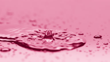 Small drop falls on big one creating ripples on pink background