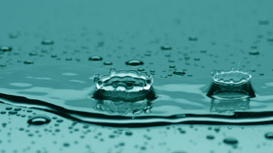 Two drops fall on big rippling one splashing on cyan background