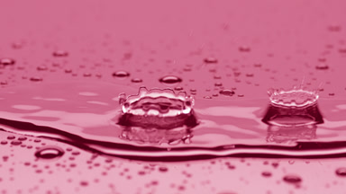 Two drops fall on big rippling one splashing on pink background