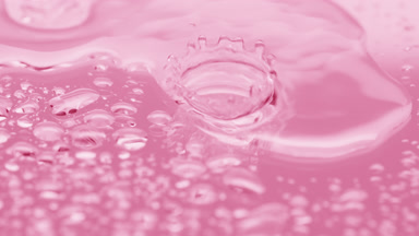 Water drops fall down on big one splashing on pink background