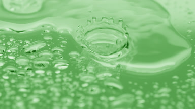 Water drops fall down on big one splashing on green background