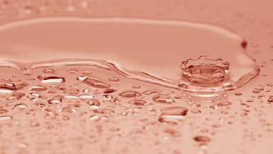 Two water drops drip on big one splashing on beige background