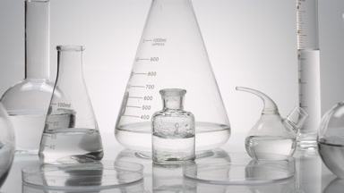 Drops drip in bottle surrounded by glassware on grey background