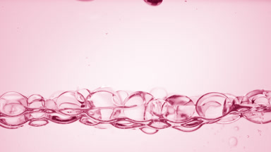 Transparent bubbles float to the surface on pale pink background