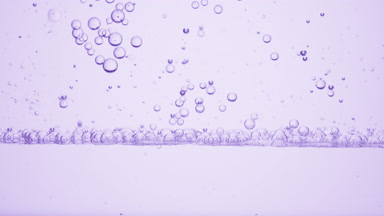 Small clear bubbles go down to the surface on purple background