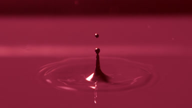Drop falls down on red opaque liquid creating circles on it