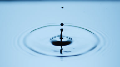 Drop drips on dark-blue opaque liquid with light reflection
