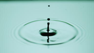 Black drop drips on green opaque liquid with light reflection