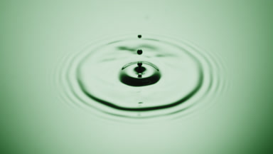 Green drop drips on green opaque fluid with light reflection