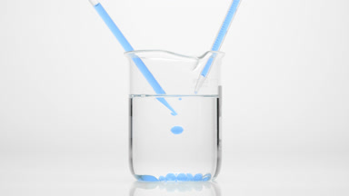 Dropper drips blue oil into water in beaker which sink to bottom