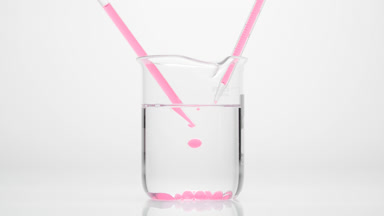 Dropper drips pink oil into water in beaker which sink to bottom