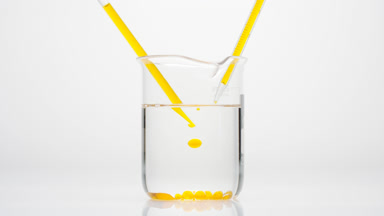 Dropper drips yellow oil in water in beaker which sink to bottom